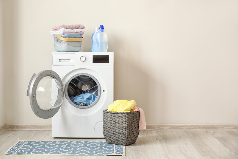 Open washing machine surrounded by laundry and detergent bottles